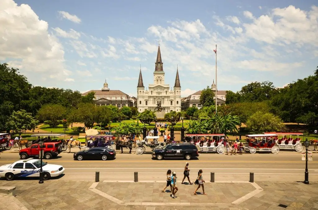 Jackson Square New Orleans with horse carriages out front and pedestrians walking in the foreground