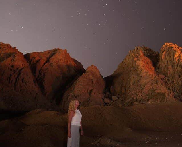 Standing in front of rocky mounds at night staring up into the stars. i am wearing a white and black skirt and white top.