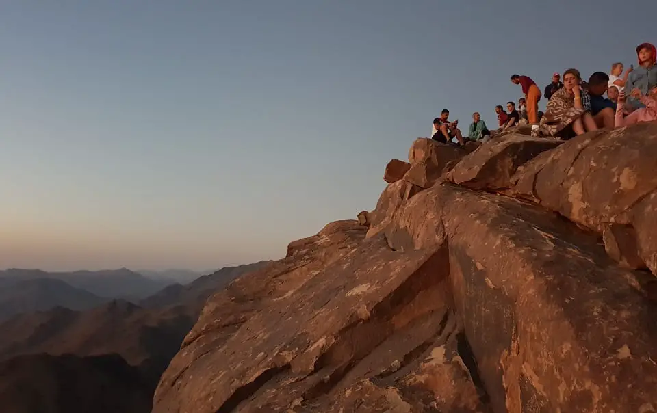 ON top of Mount Sinai, a group of people sitting on a rock ledge looking out. 