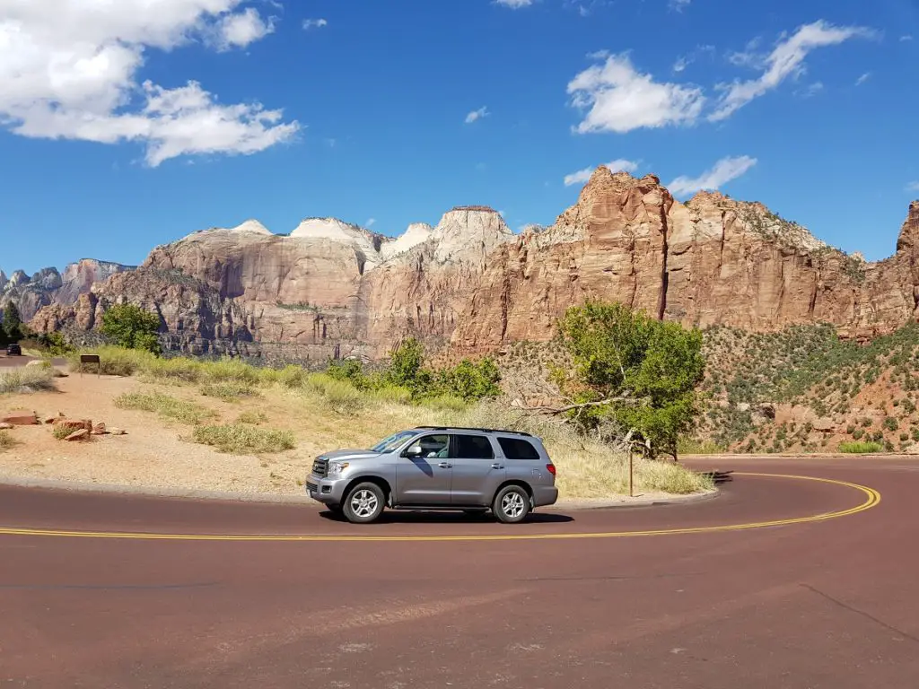 Visiting America for the first time - on a road trip with desert background and car on road 