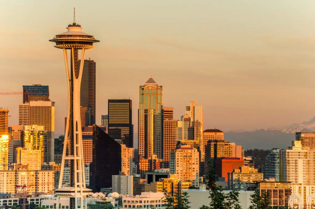travel USA on a budget = Seattle skyline at sunset shows a golden hue surrounding the city