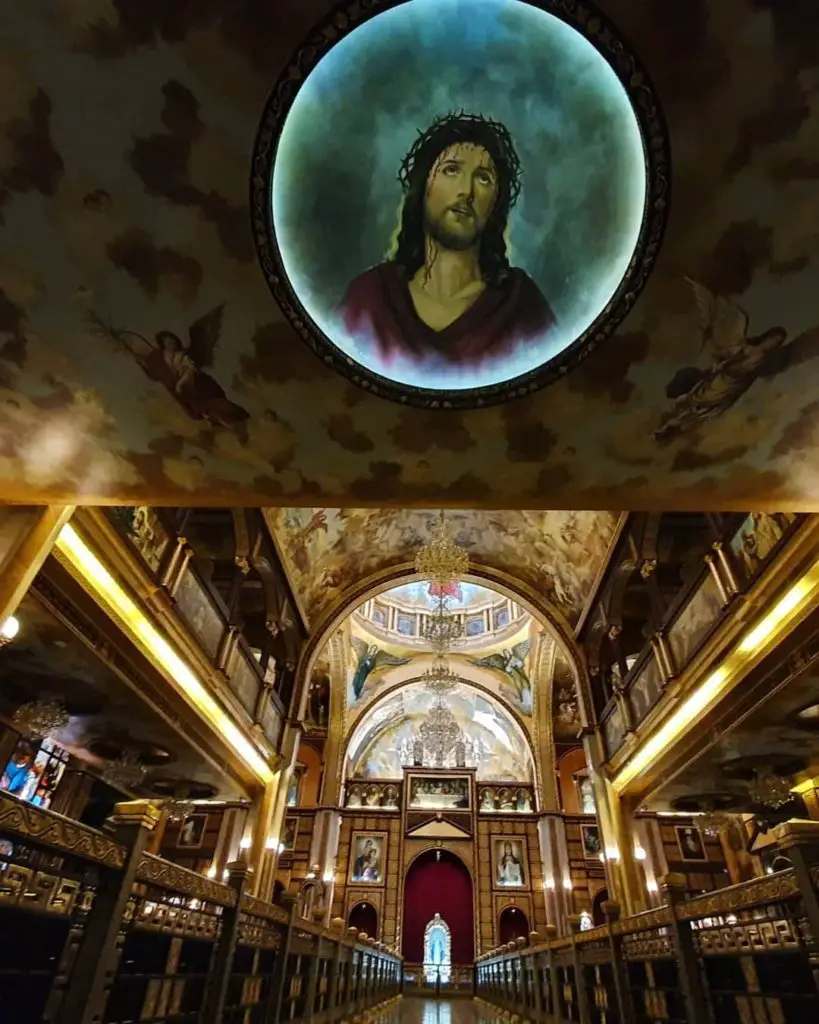 Ornate interior of coptic church in Egypt. Paintings adorn the wallls and a painting of Jesus on the roof.