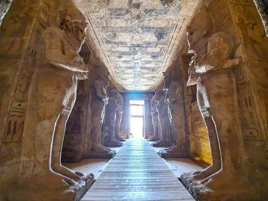 inside Abu Simbel looking down a corridor that leads to the outside light. Tall statues adorn the hallway on either side.