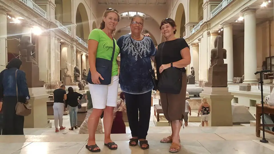 Three ladies posing for a photo in the Egyptian museum with artifacts behind