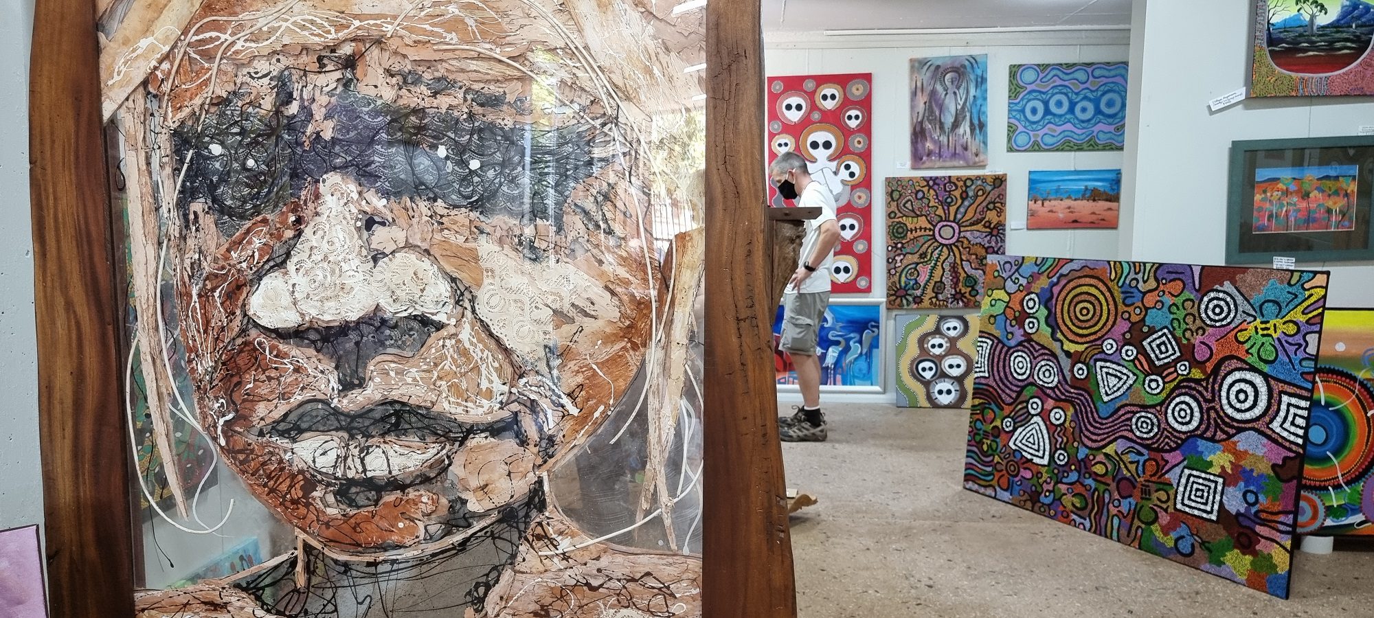 painting of an indigenous person with colorful works in the background at Norval Gallery